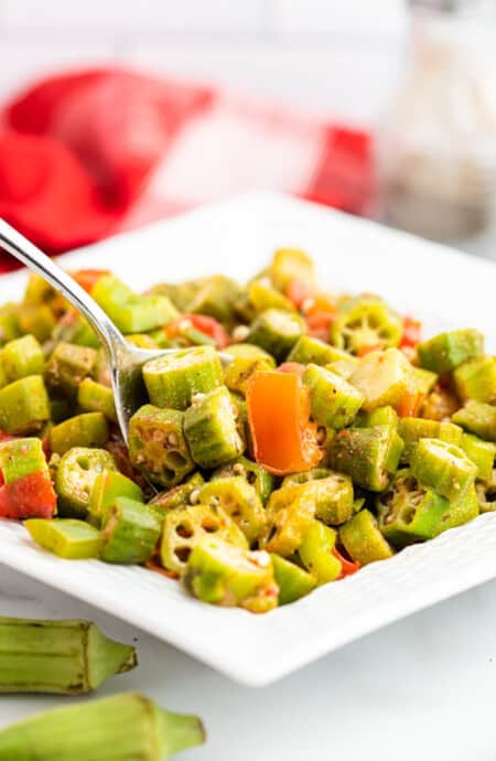 close up of white dish of okra and tomatoes with a spoon