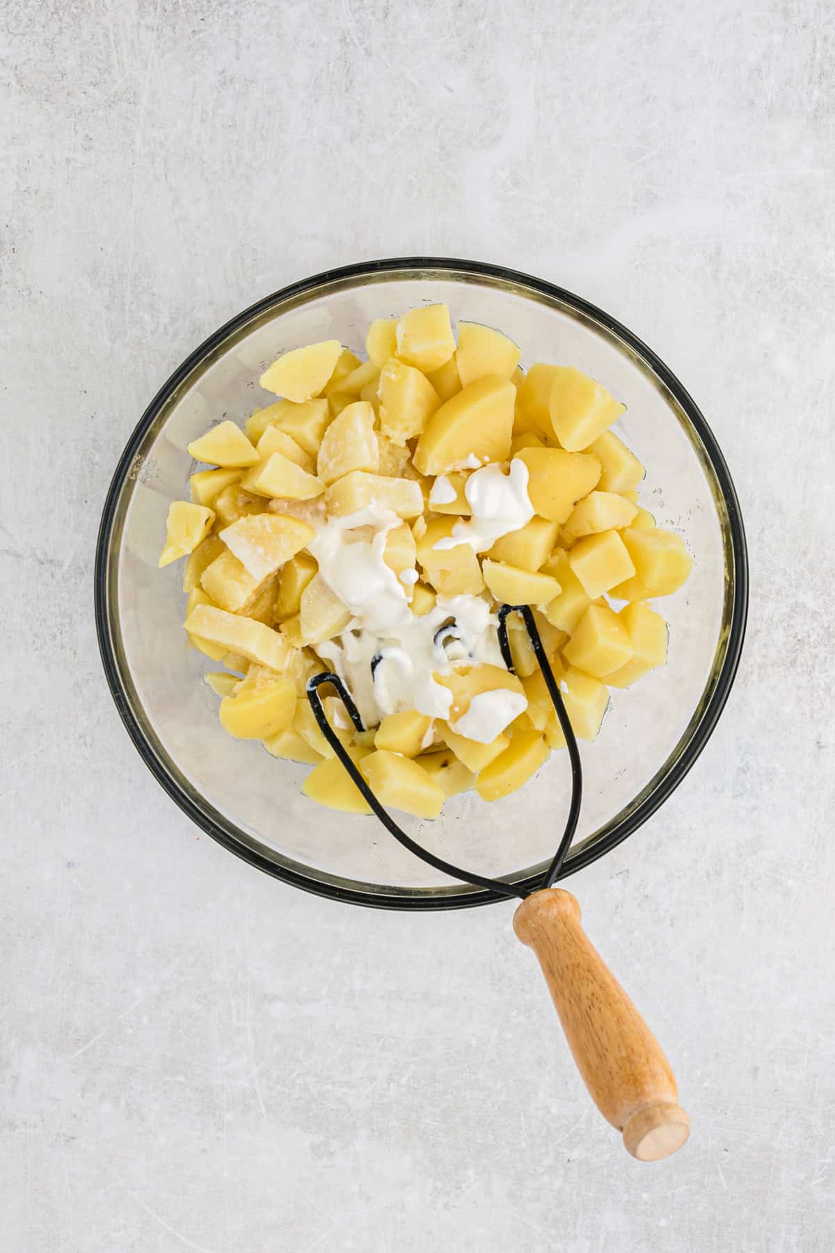 Yukon gold potatoes in a glass bowl with a masher on white background