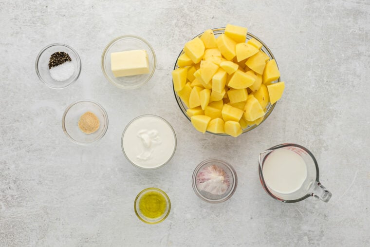 Potatoes, sour cream, butter, oil, seasonings in glass bowls on white countertop