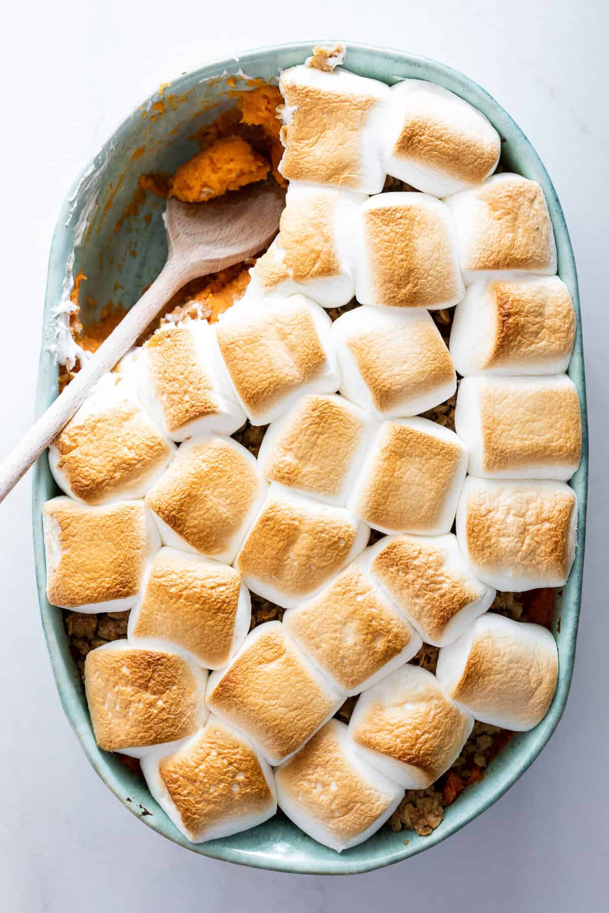 a spoon digging into a sweet potato casserole on a white background