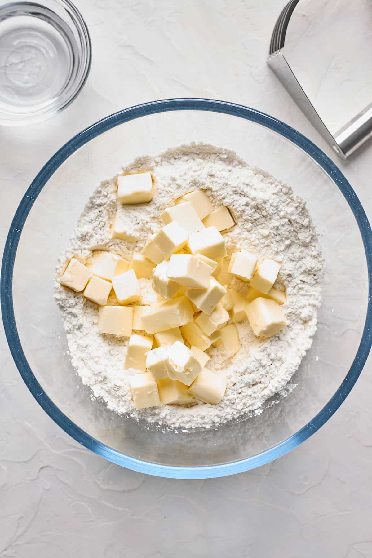 Cubed butter in flour mixture in glass bowl on white countertop