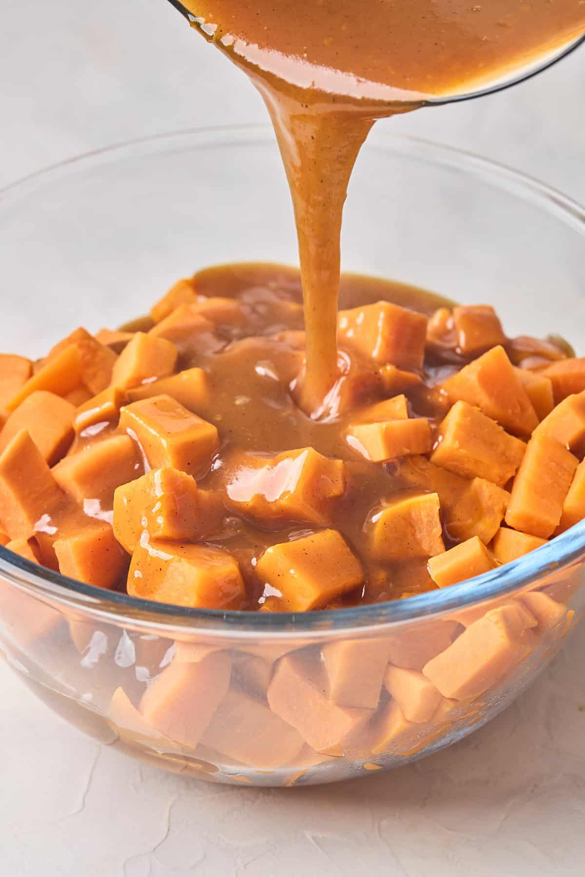 Cobbler syrup being poured over boiled tender sweet potatoes in a glass bowl