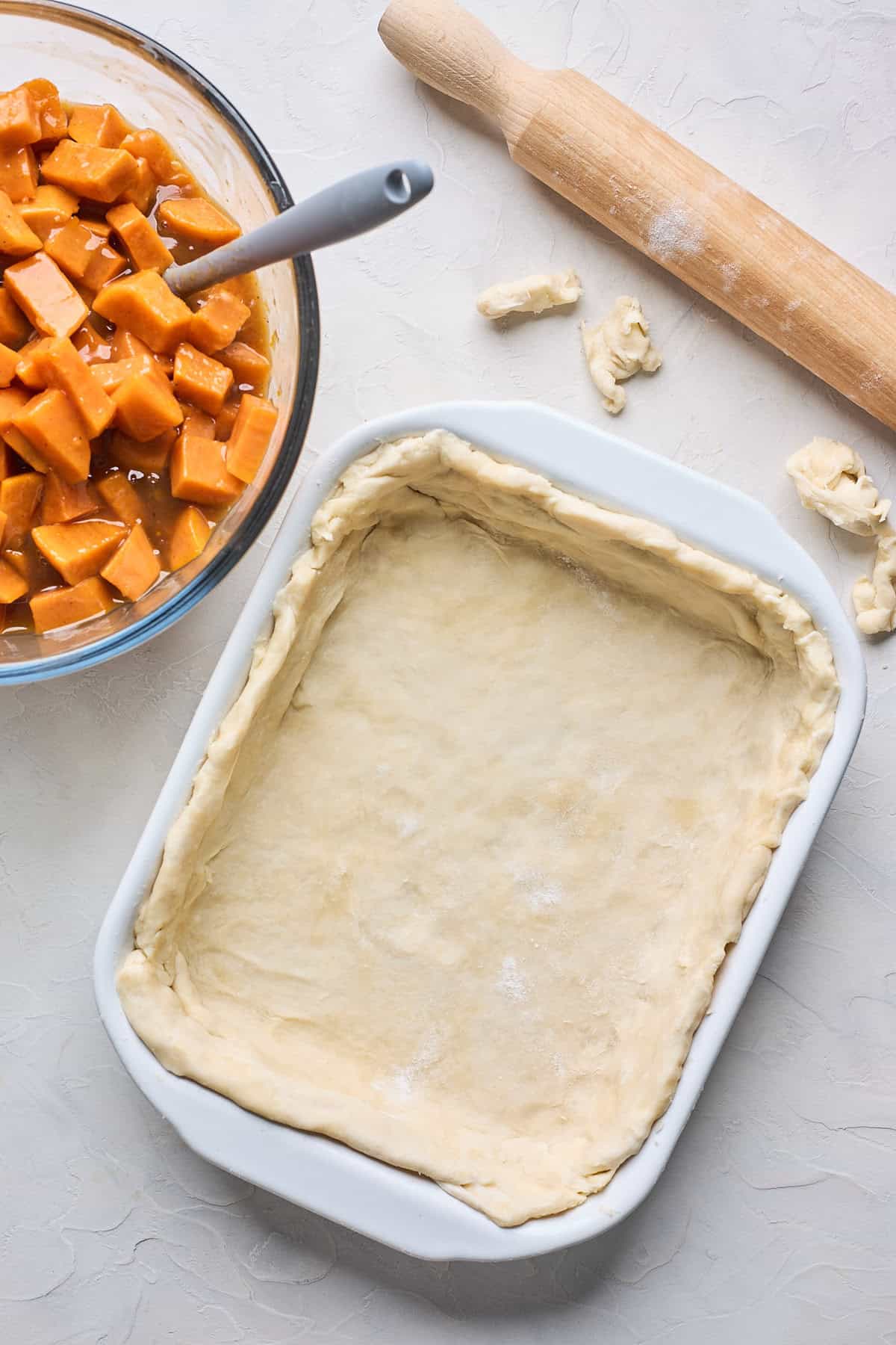 Crust added to a baking casserole dish with a sweet potato filling on the side with a rolling pin on the side as well