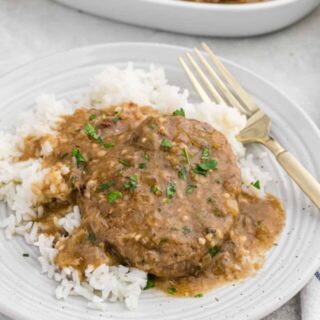 Smothered round steak over white rice with a gold fork on a dinner plate.