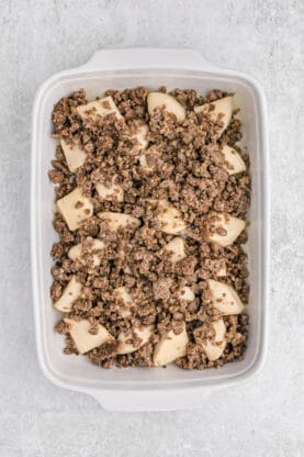 Crumbled sausage over biscuit pieces in a casserole dish