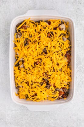 Shredded cheese over sausage and biscuits in a casserole dish