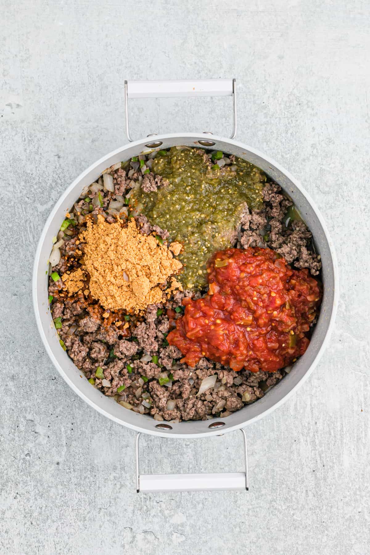 Browned ground beef in a skillet with red and green salsa and taco seasoning