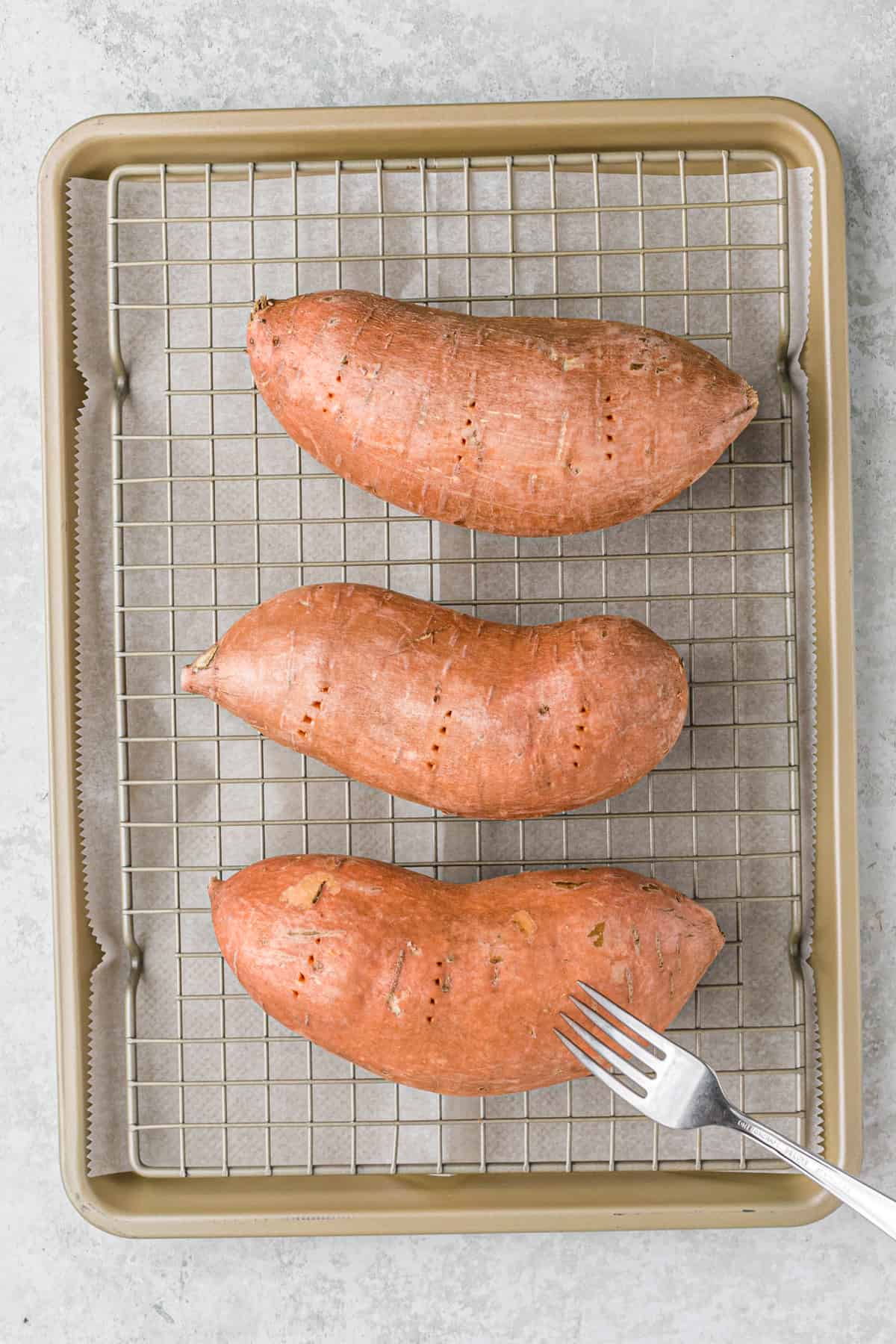 A fork poking holes in sweet potatoes on a wire rack.