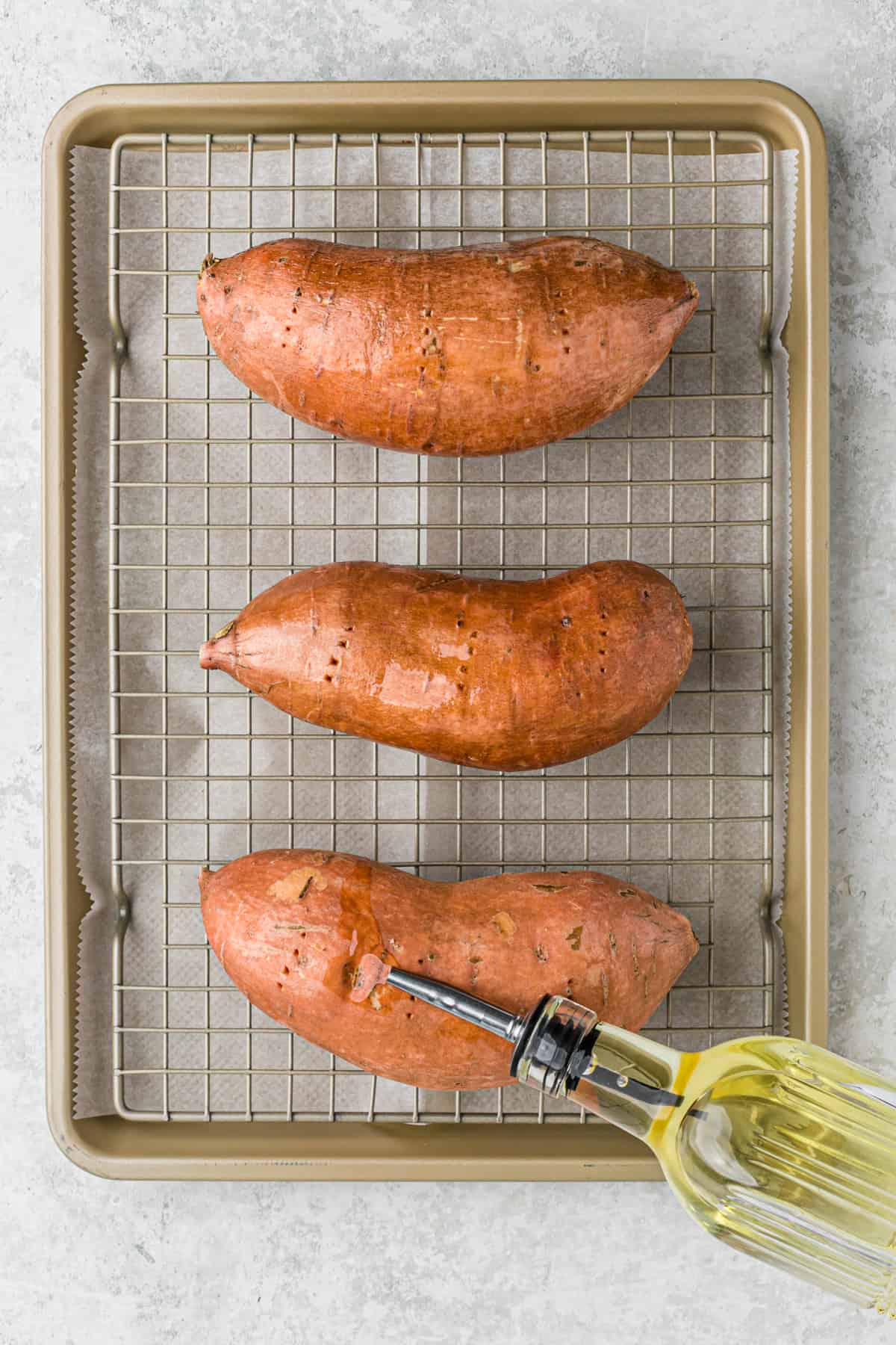 Drizzling olive oil over sweet potatoes on a wire rack in a baking sheet.