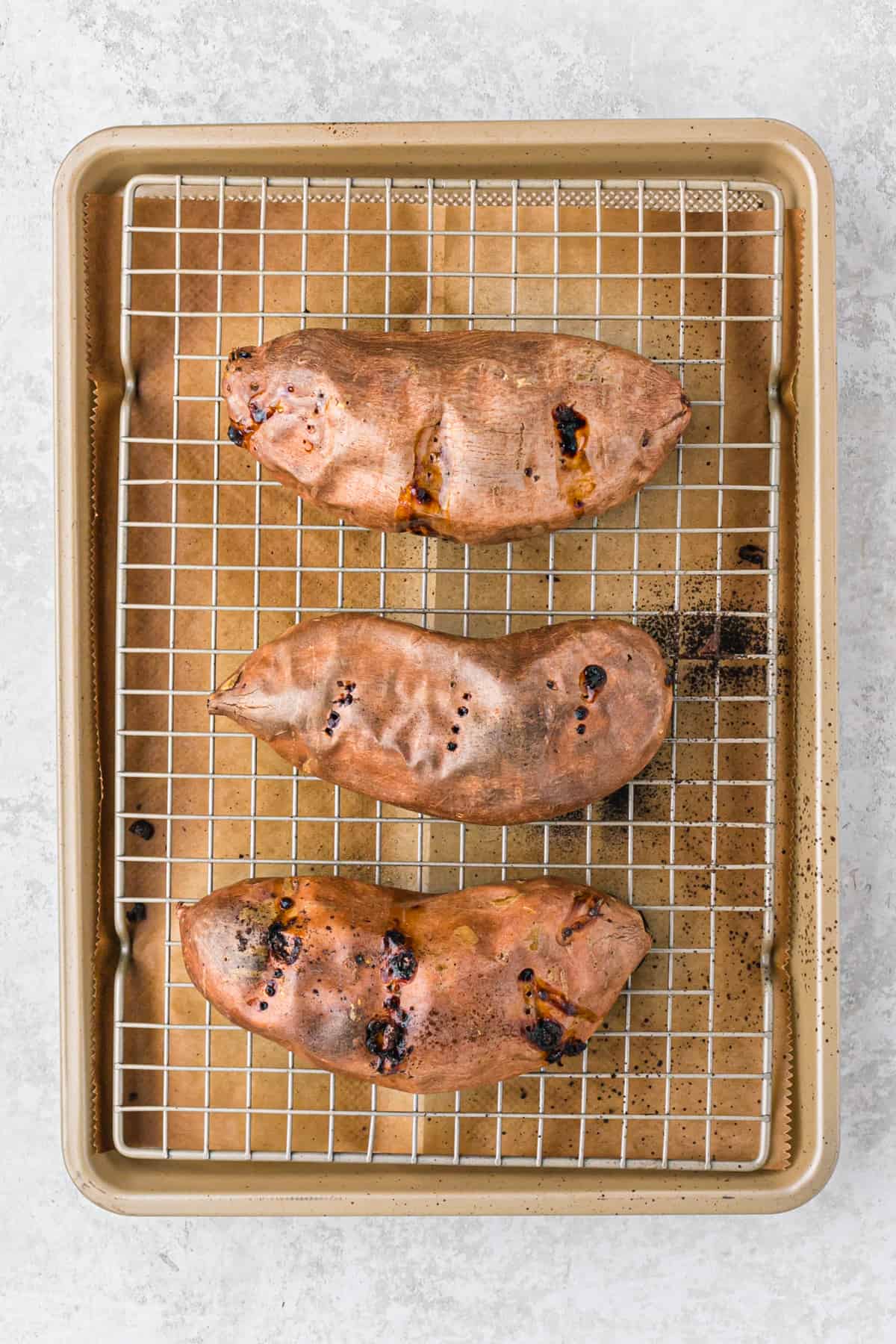 Baked sweet potatoes on a rack in a baking sheet.