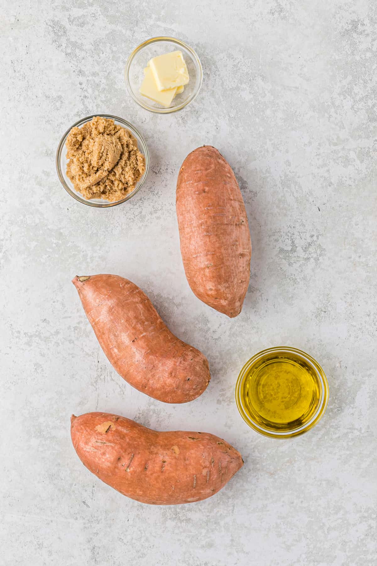 Sweet potatoes and bowls of brown sugar, oil, and butter on a counter.