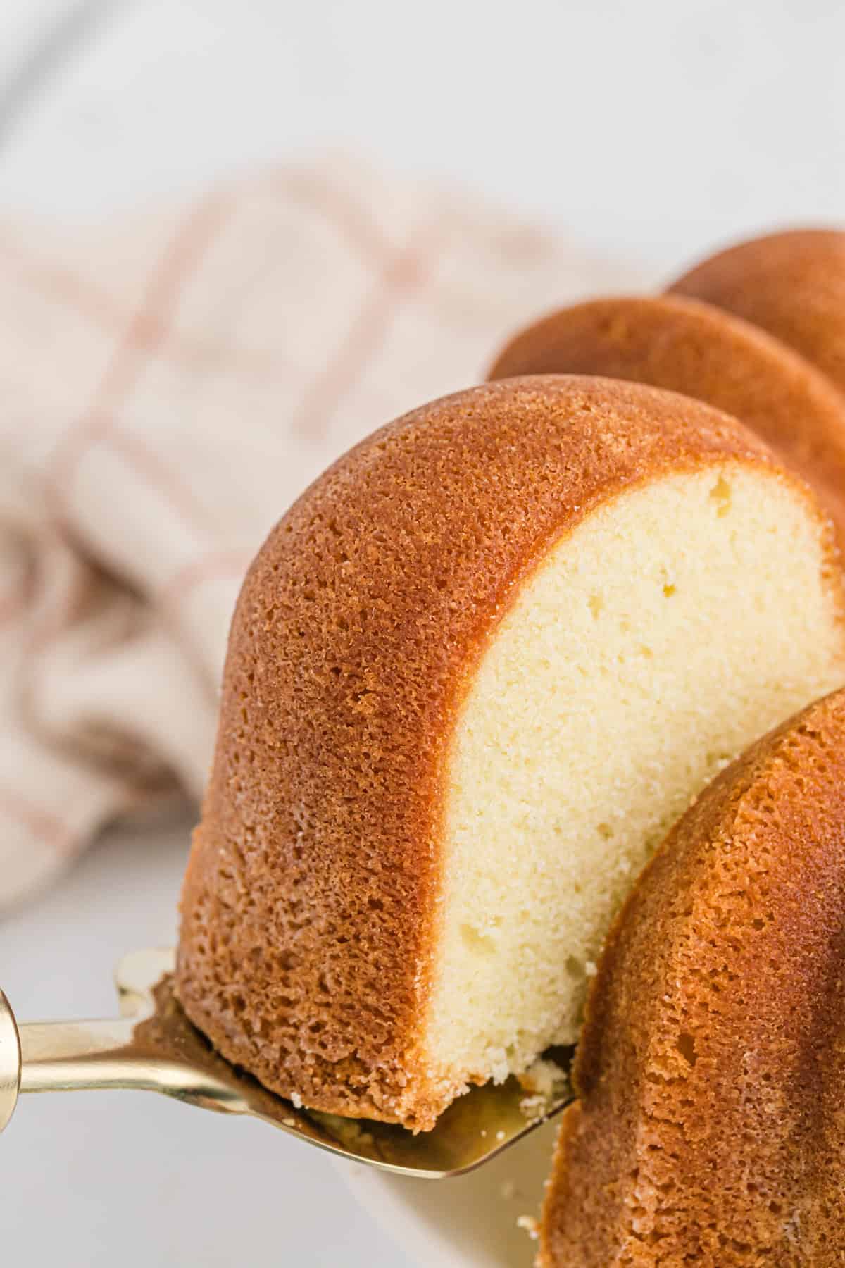 A slice of pound cake made with sour cream being lifted from the cake on white background with striped napkin in background