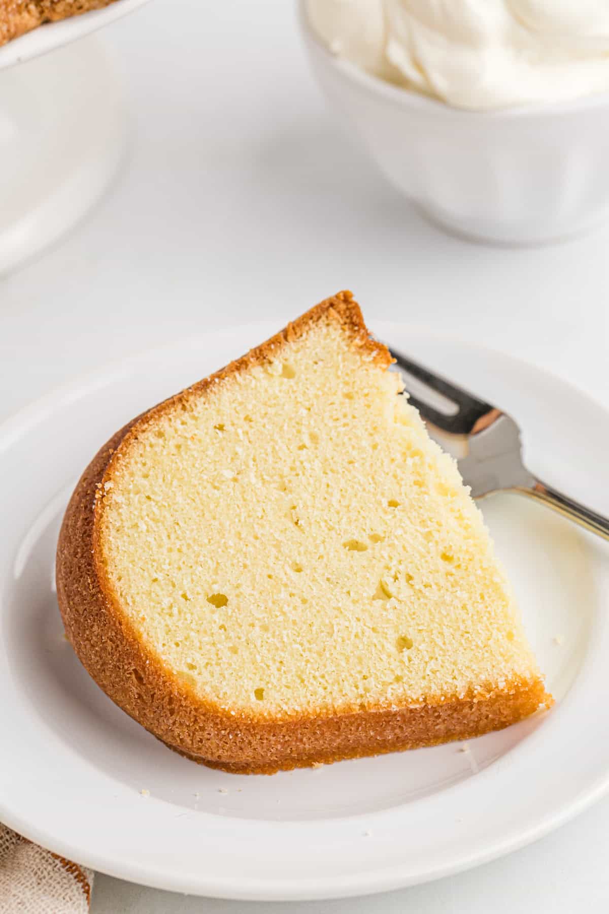 A perfect slice of a pound cake with sour cream on a white plate with a silver fork