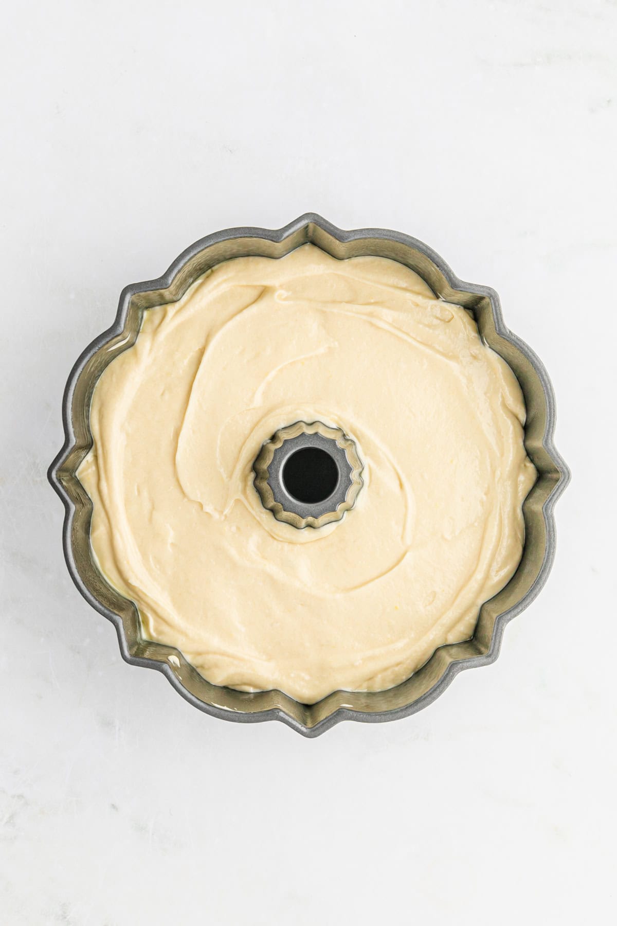 Cake batter in a greased bundt pan on white countertop