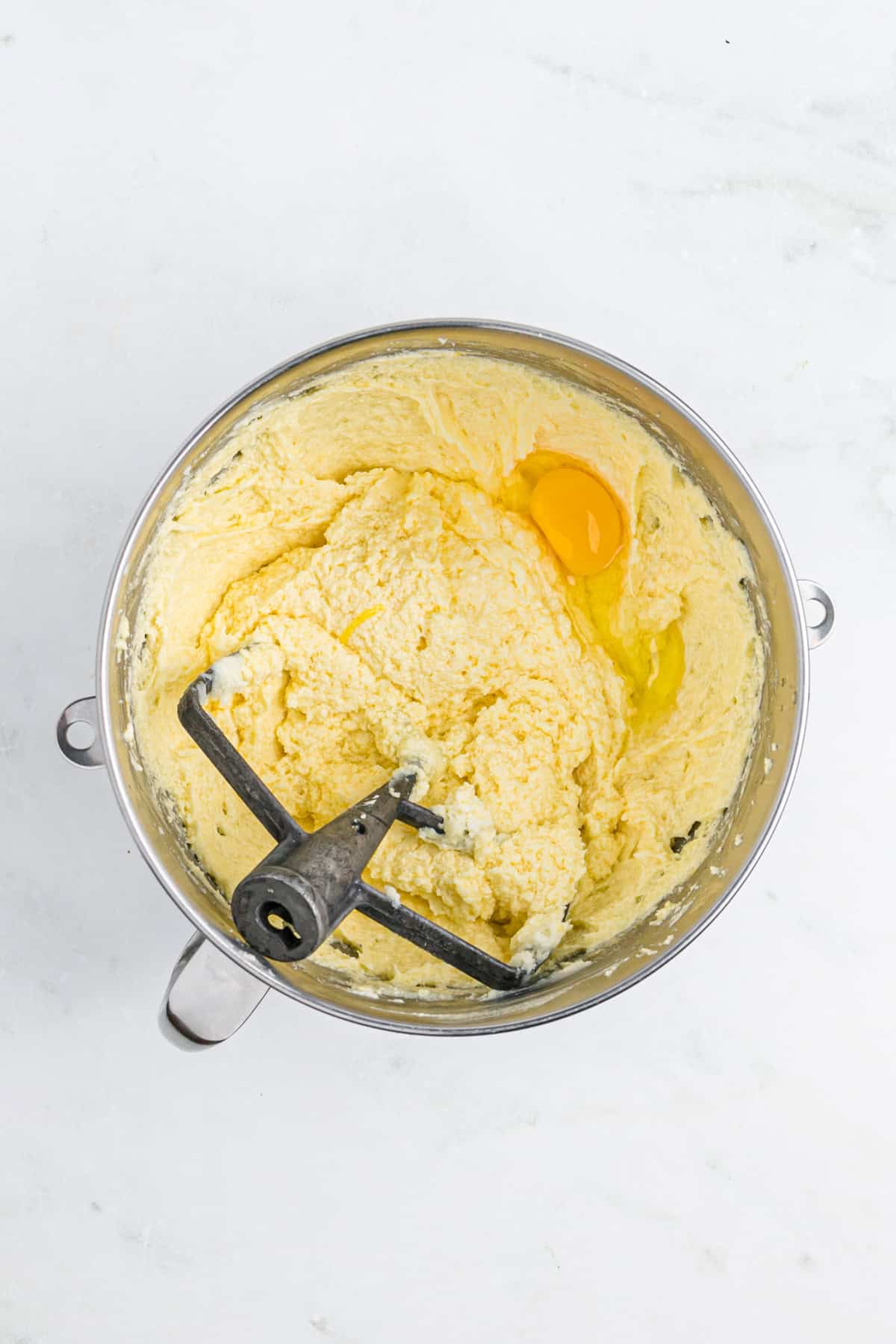 Eggs added to a creamed butter and sugar mixture in a stand mixer bowl on white countertop