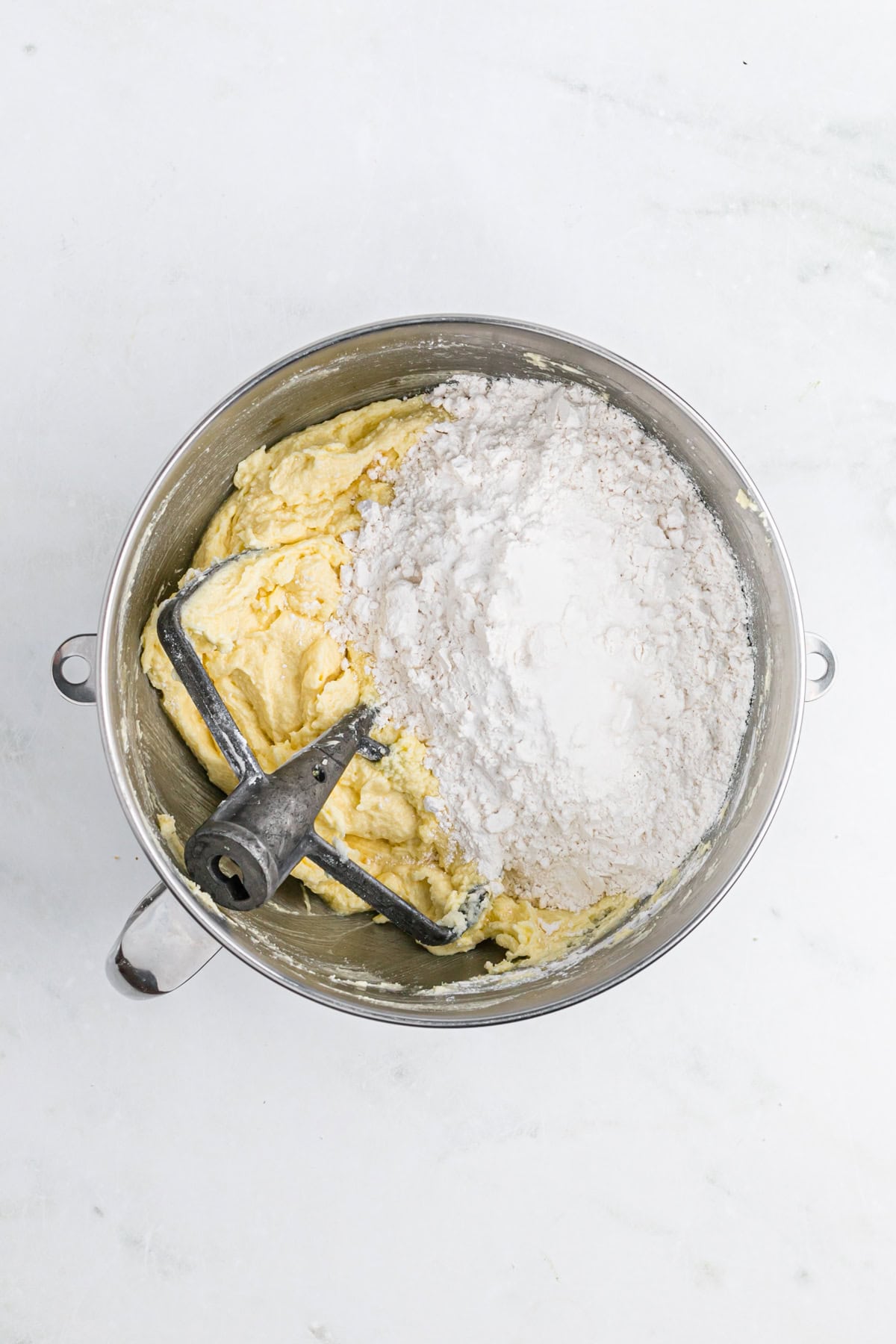 Dry ingredients added to a sour cream pound cake batter in a stand mixer on a white countertop