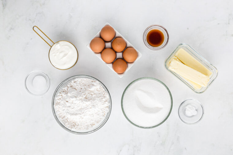 Flour, butter, eggs, sugar and vanilla in glass bowls on white countertop