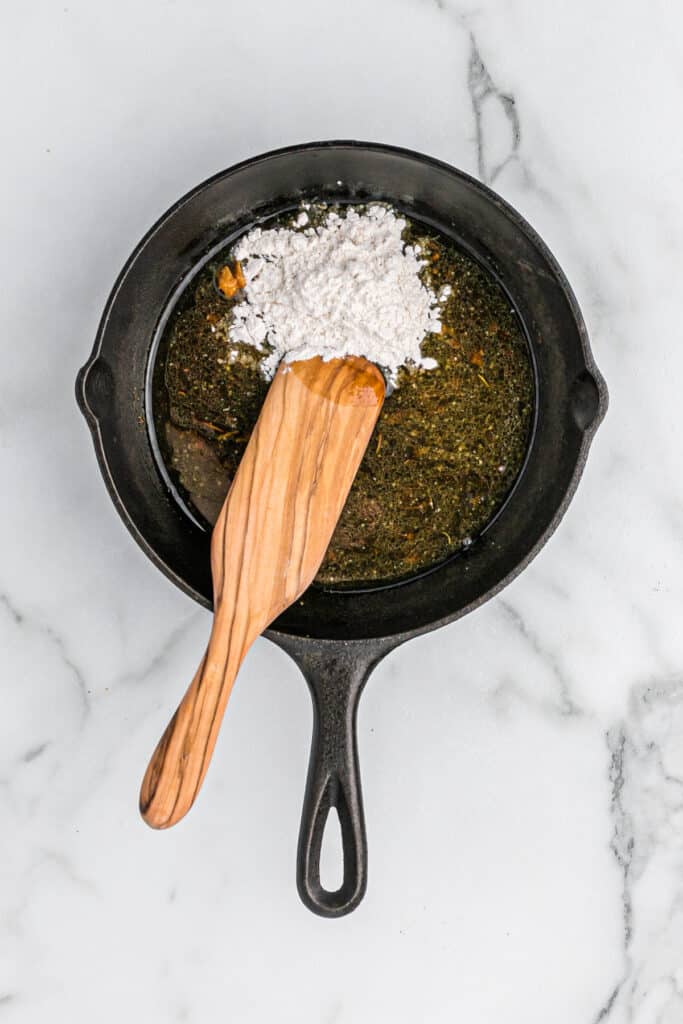 A wooden spoon stirring flour into turkey drippings in a cast iron skillet on white countertop