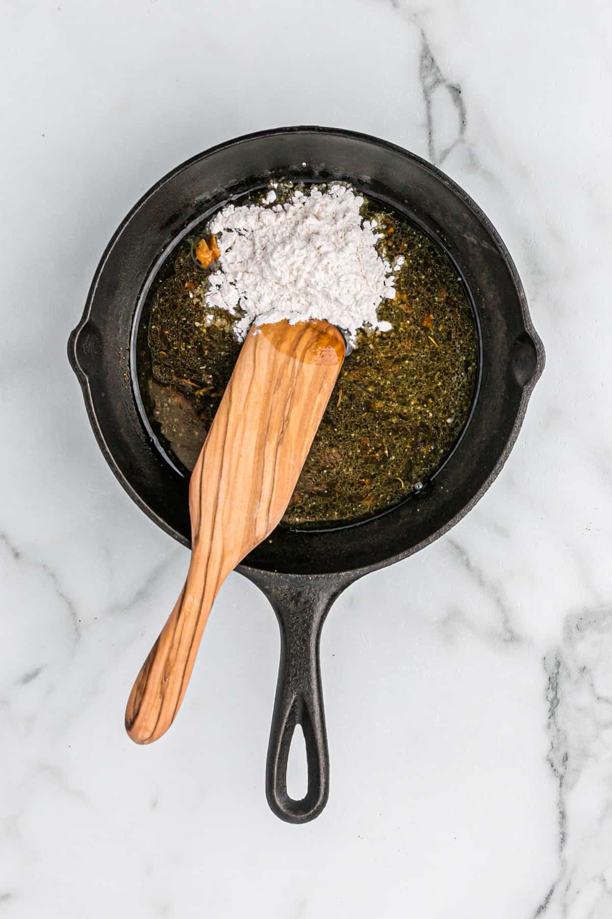 A wooden spoon stirring flour into melted butter in a cast iron skillet.