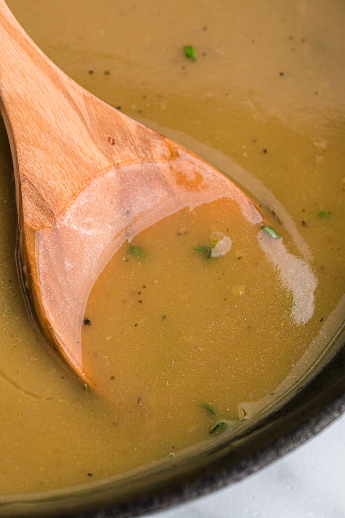 A wooden spoon in a saucepan of turkey gravy.