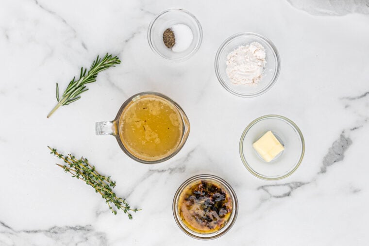 Stock, seasonings, butter, turkey drippings in glass bowls on white countertop