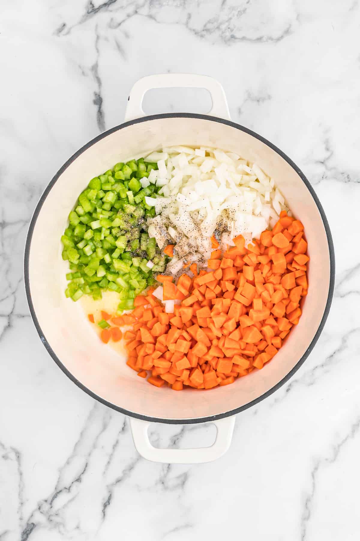 Celery, carrots and onion being sauteed in a large pot on white countertop