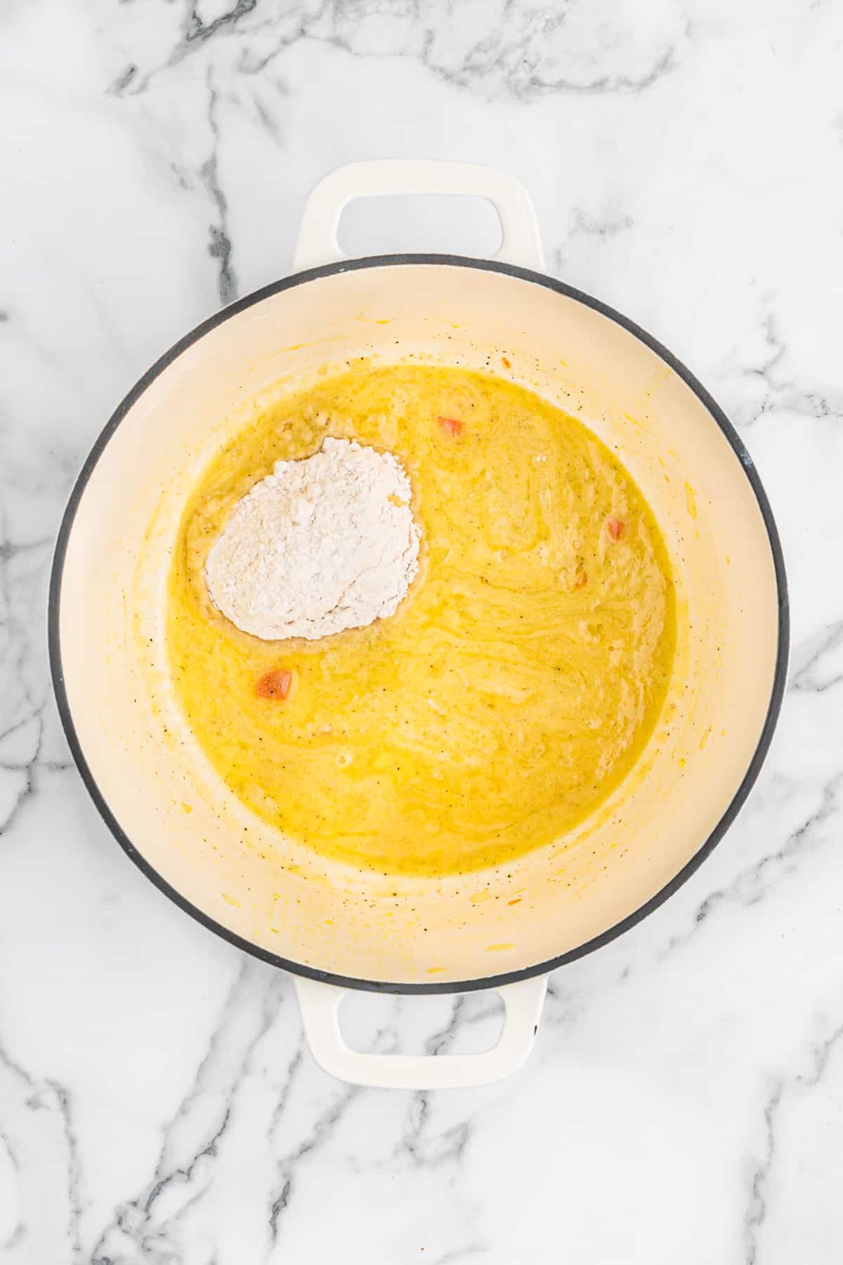 Flour added to butter in a large pot on white countertop.