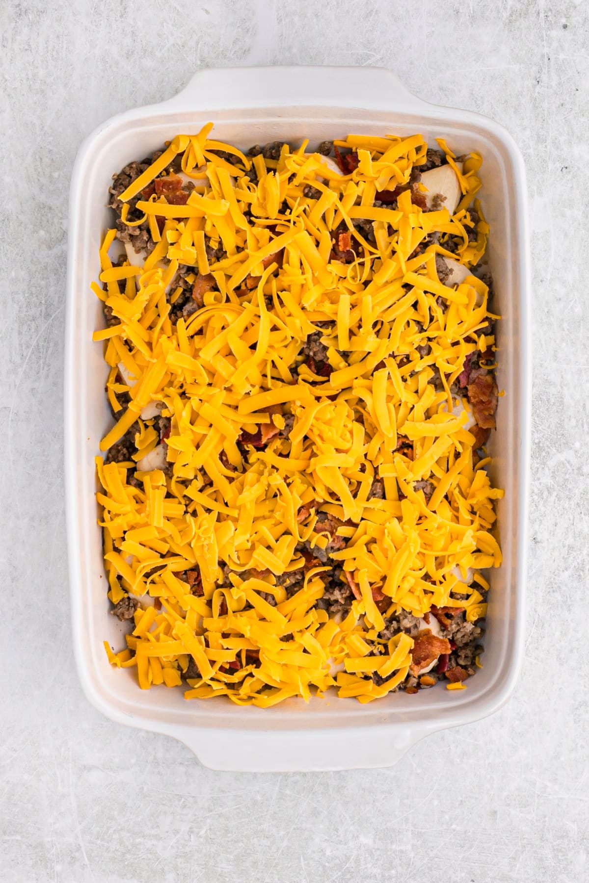 A generous layer of shredded cheddar cheese covering the sausage and biscuit mixture