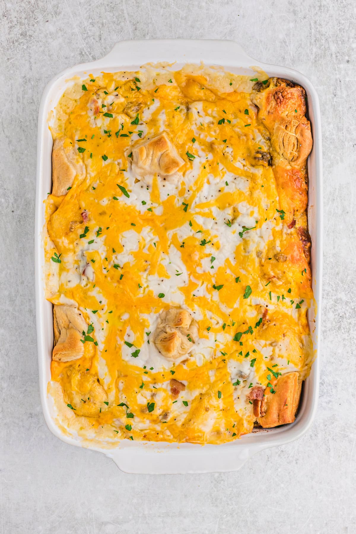 Fully baked biscuits and gravy casserole with golden biscuits peeking through melted cheese and gravy, sprinkled with chopped parsley