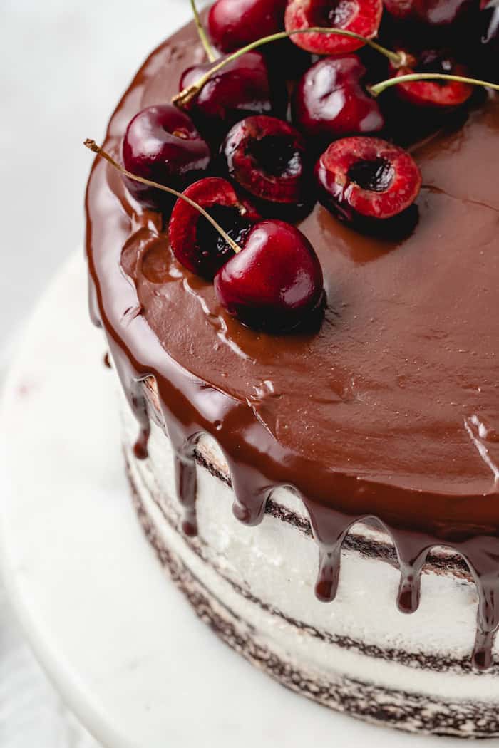 An iced and garnished black forest cake recipe on a white cake stand ready to serve