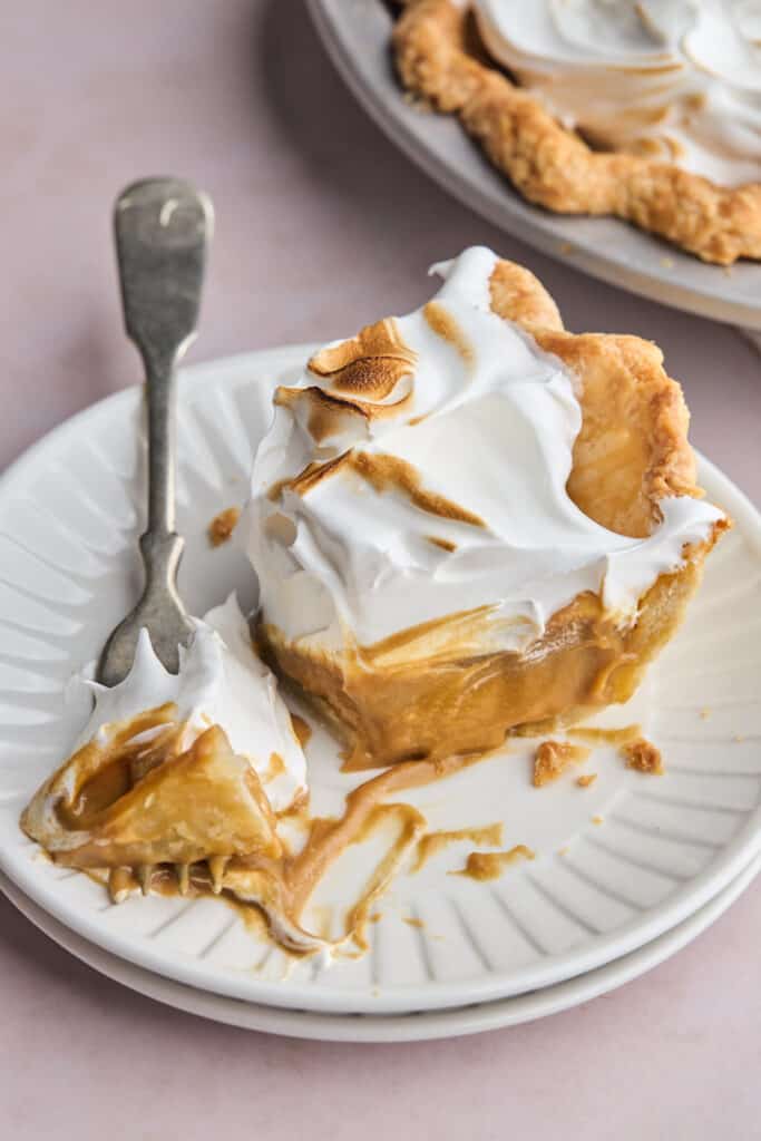 a bite being taken out of a piece of butterscotch pie with a fork on a plate
