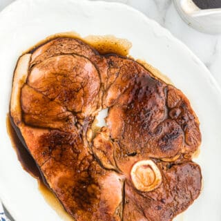 A ham steak with red eye gravy on a white dinner plate.