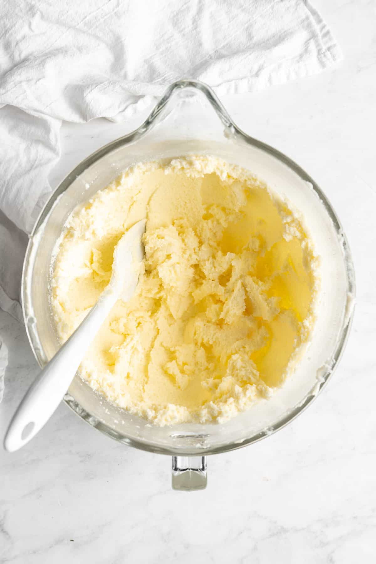 Butter and sugar in stand mixer bowl with a spatula mixing on white countertop