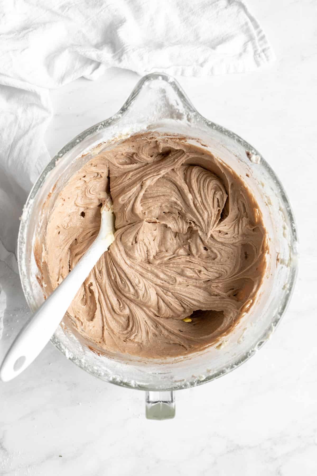 Red velvet bundt batter being mixed in a stand mixer bowl on white countertop