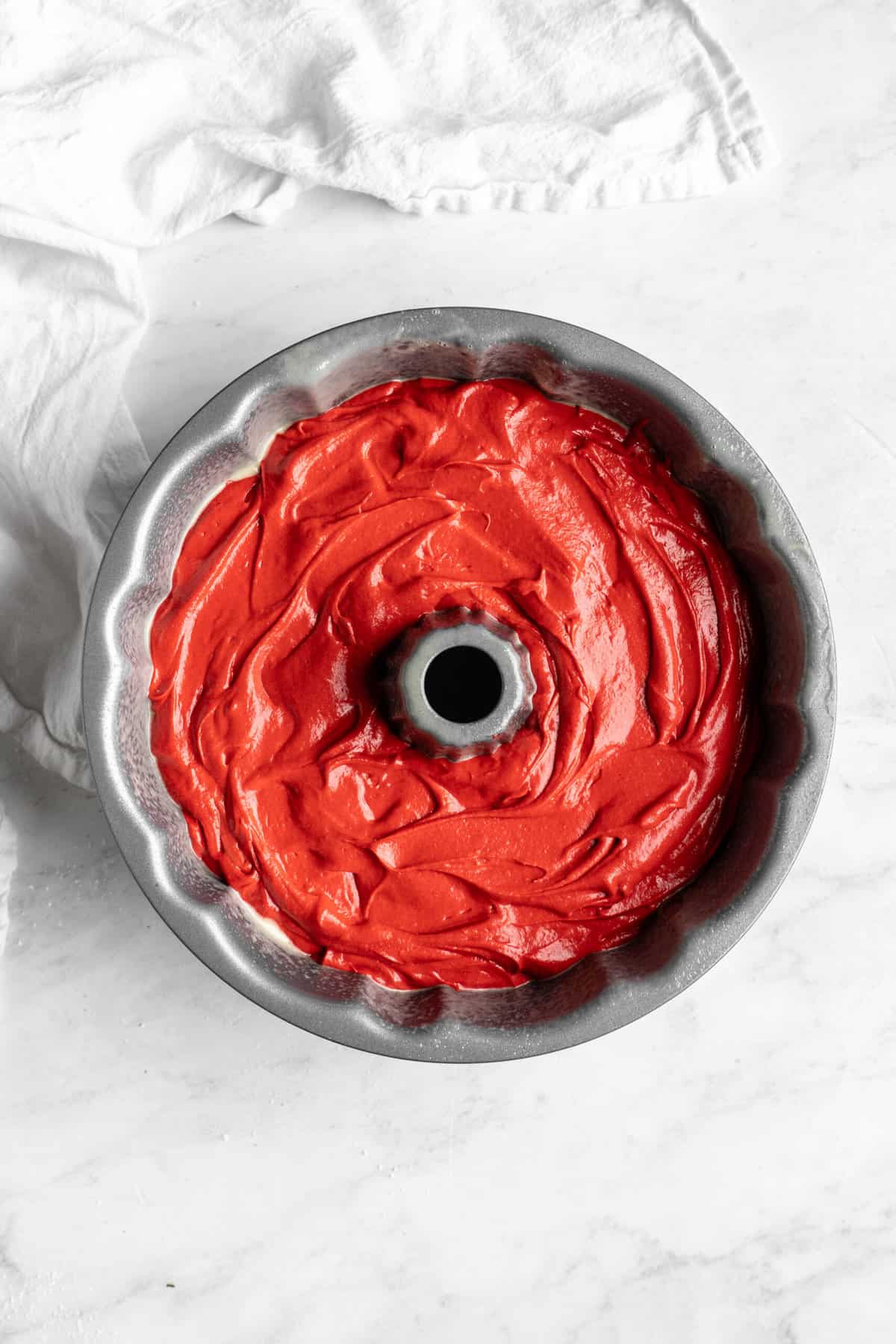 Red velvet bundt batter added to a bundt pan on white background