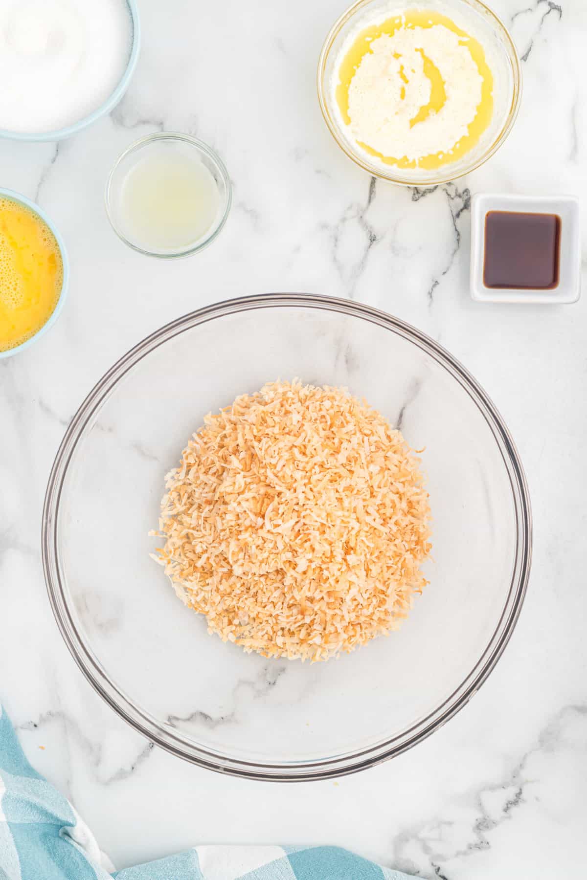 Toasted coconut in a large mixing bowl with other ingredients in small bowls.