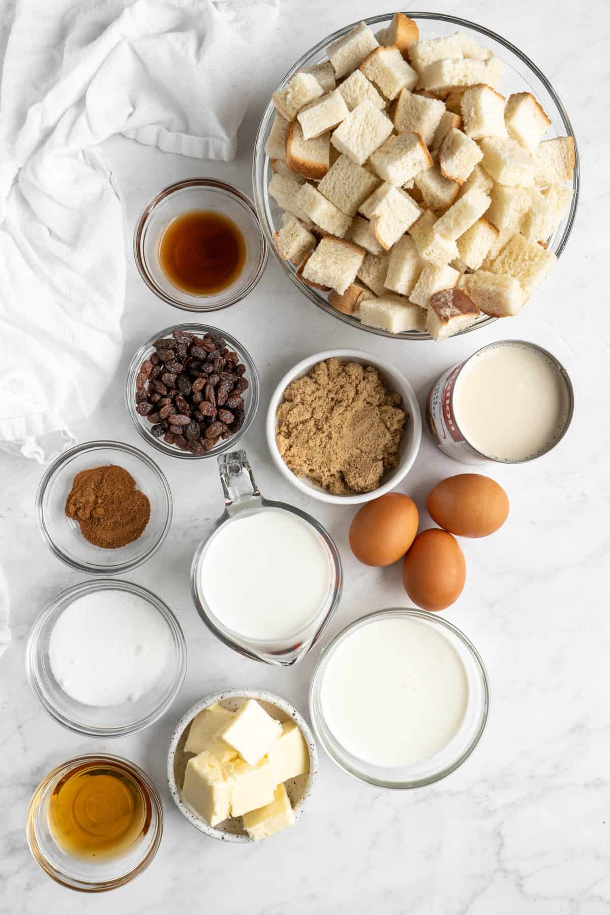 Ingredients to make classic bread pudding in small bowls on a white surface.