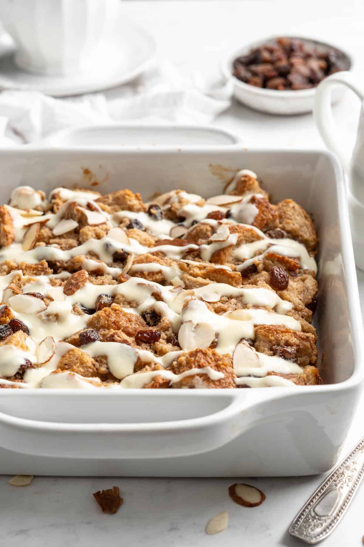 A white square baking dish of bread pudding with raisins.