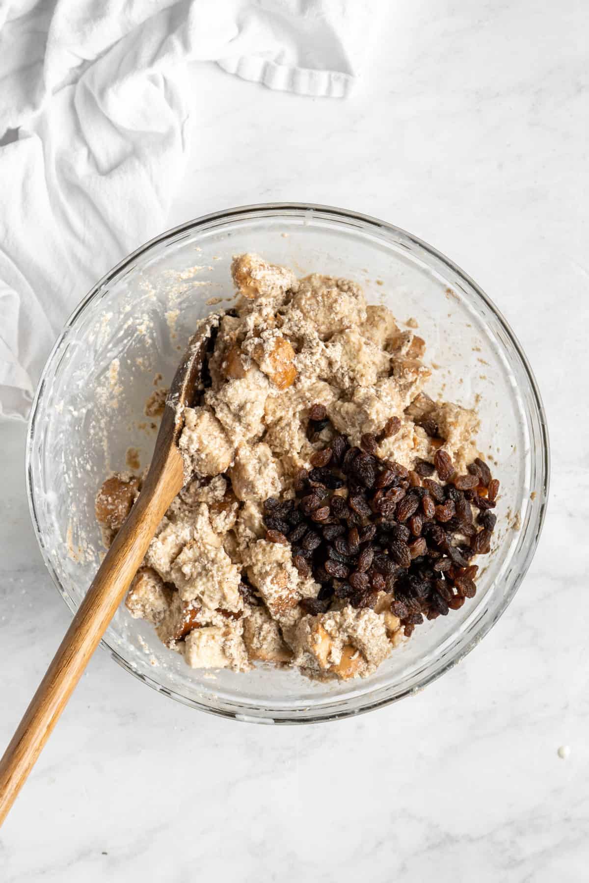 A wooden spoon in a mixing bowl of bread pudding with raisins.