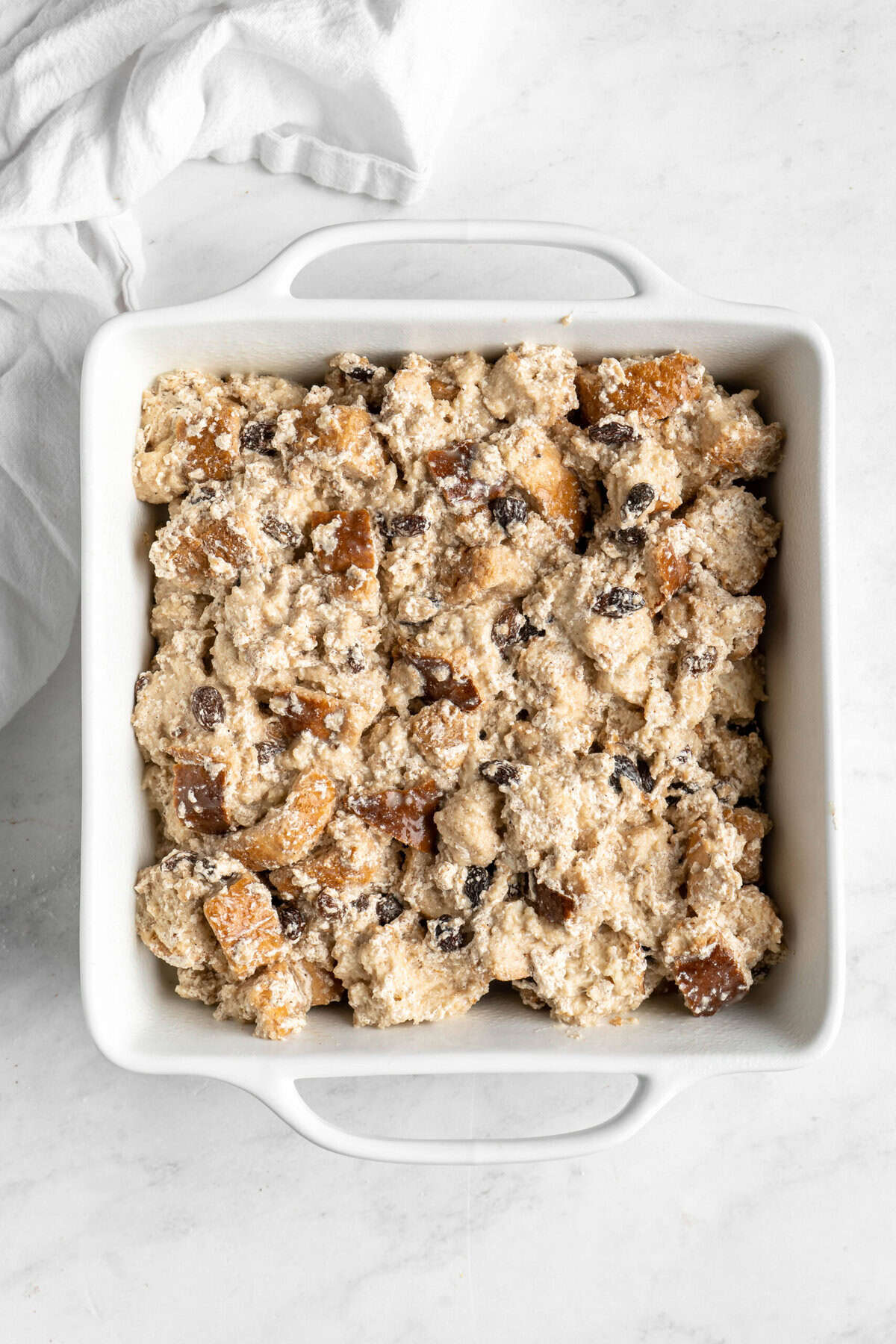 Bread pudding before being baked in casserole dish on white countertop.