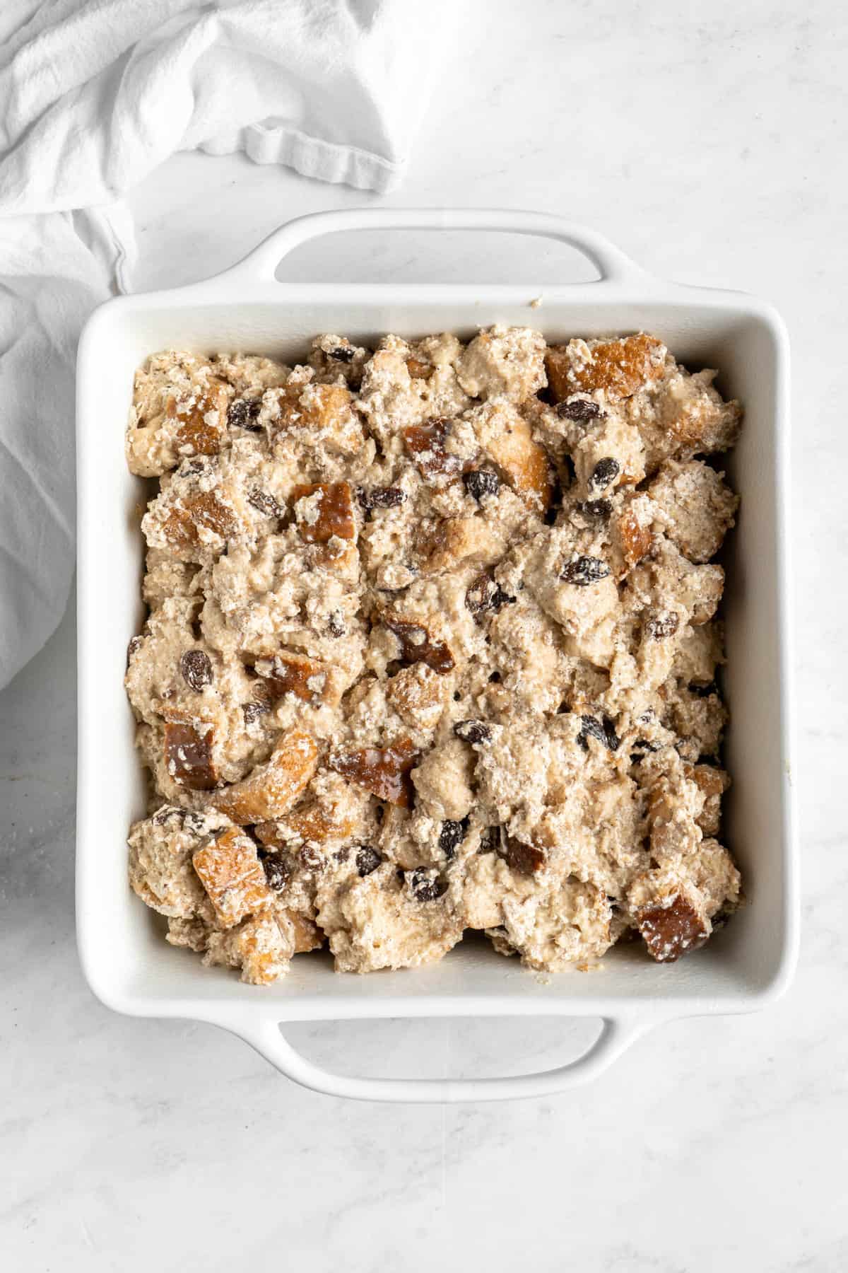 Unbaked bread pudding in a white square baking dish.