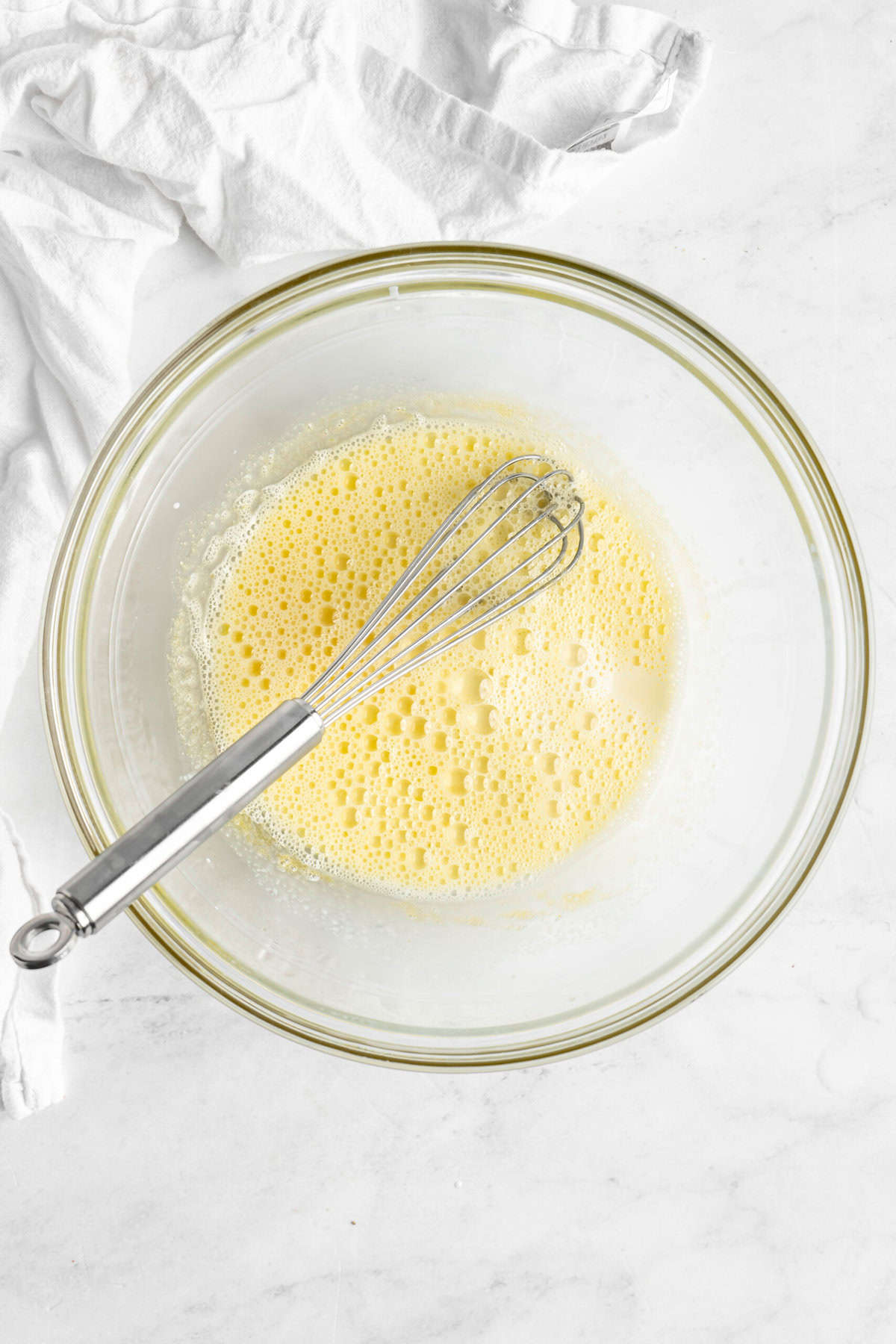 Eggs being whisked in a glass bowl on white countertop