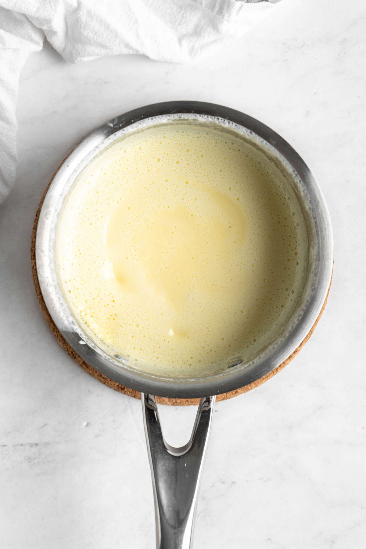 Cream sauce for old fashioned bread pudding in pot on white countertop