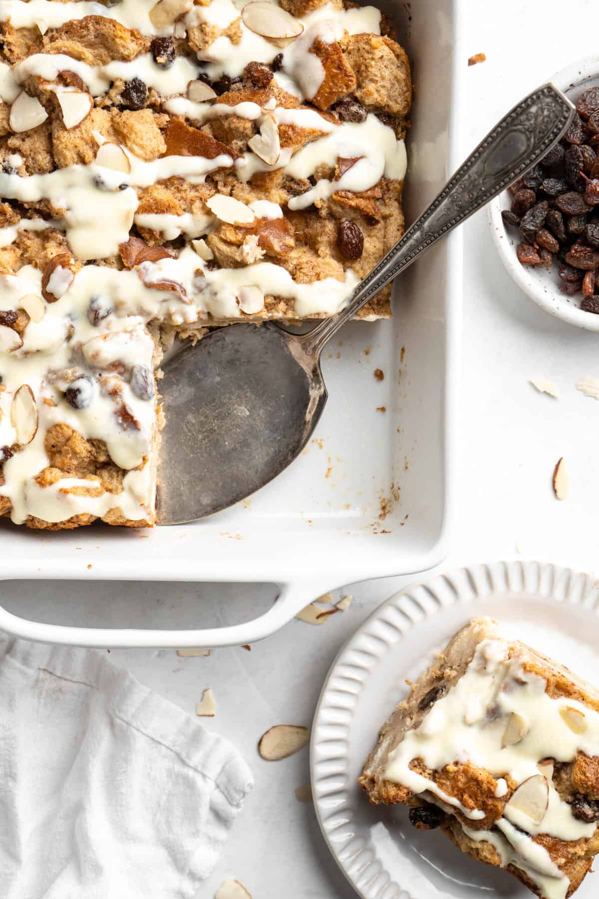 Bread pudding in a baking dish with a slice removed to a plate.