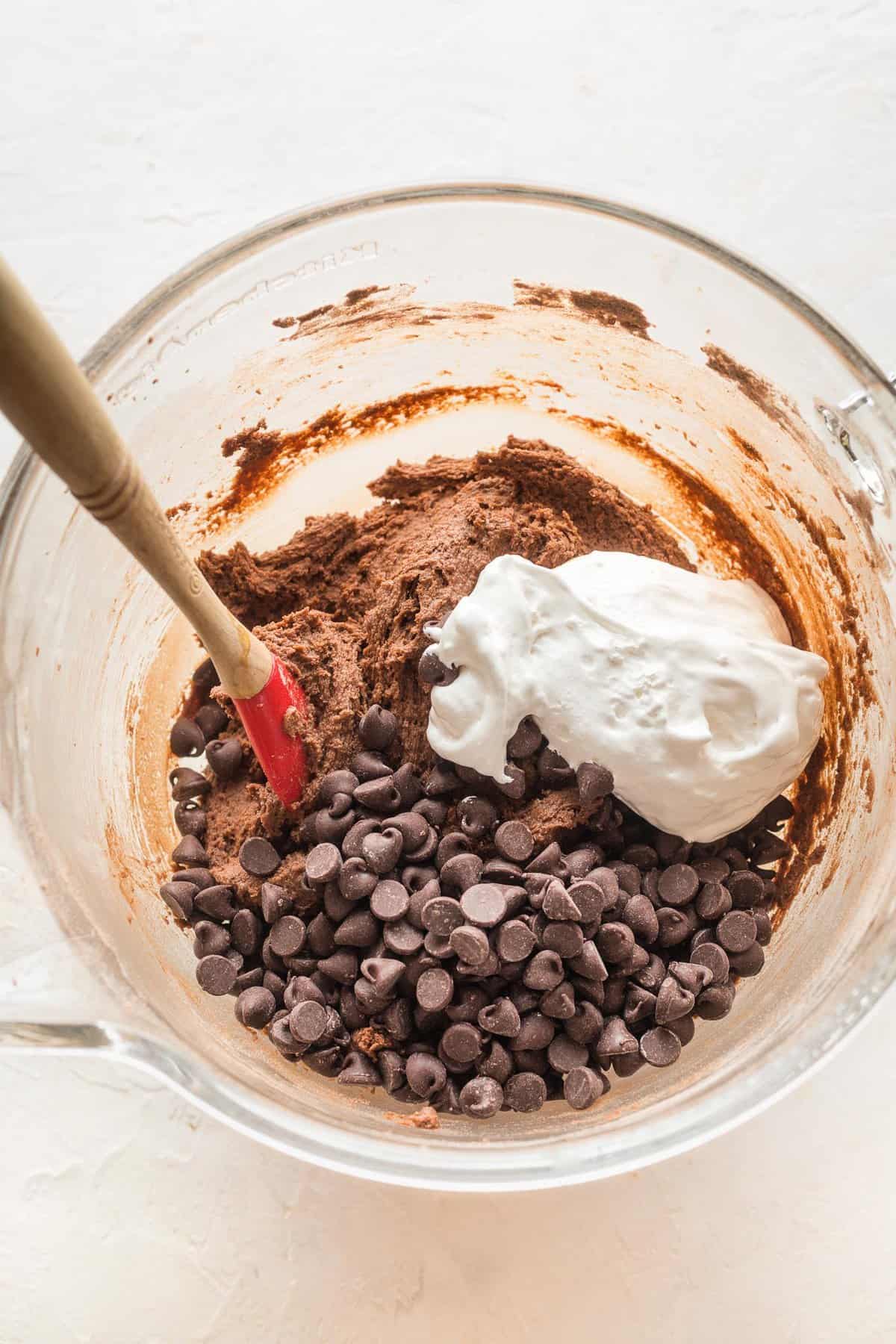 Chocolate chips and marshmallow fluff on top of chocolate cookie dough in a bowl.