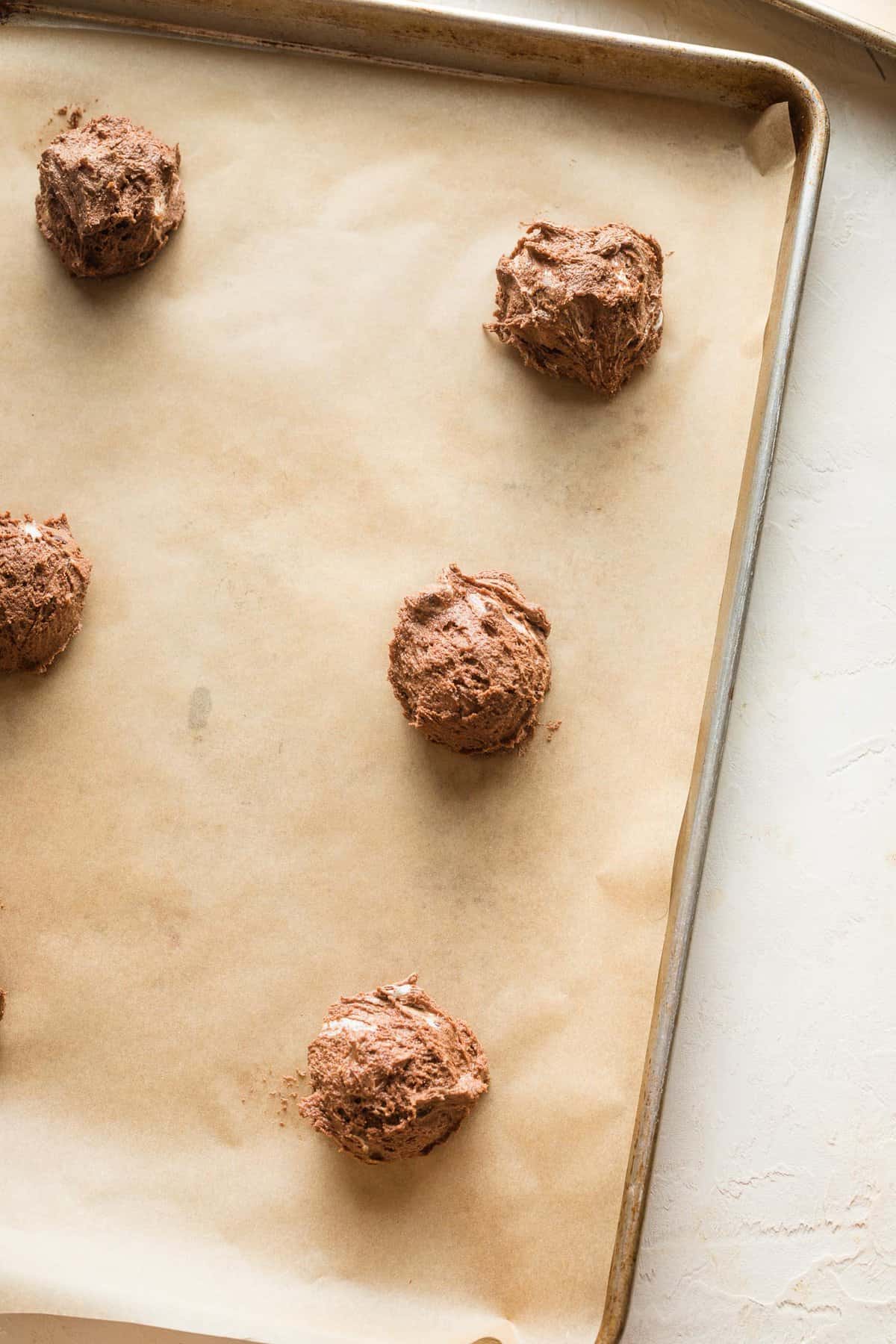 Hot chocolate cookie dough balls on a parchment lined baking sheet.
