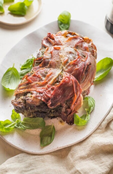 A white serving platter with a prosciutto wrapped beef roast.