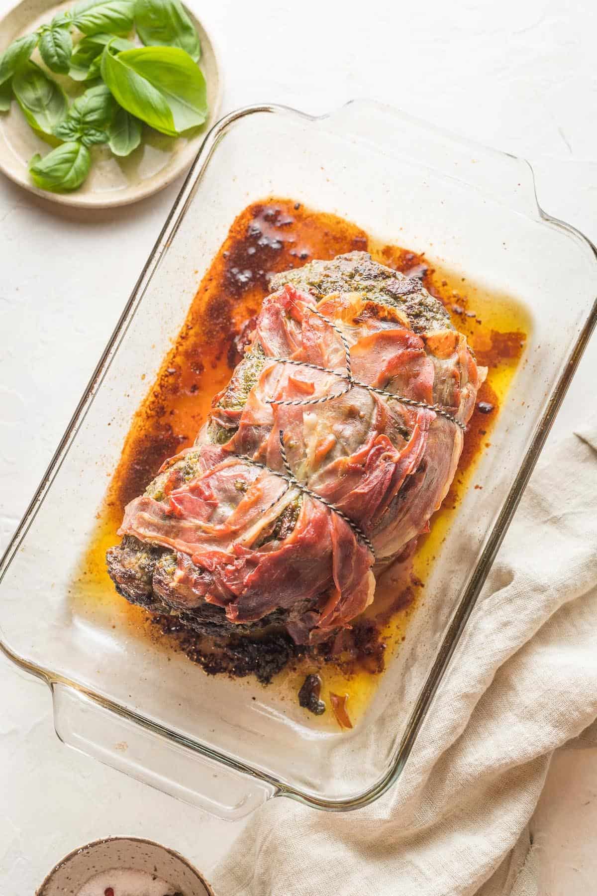 A prosciutto wrapped beef roast in a glass baking dish.