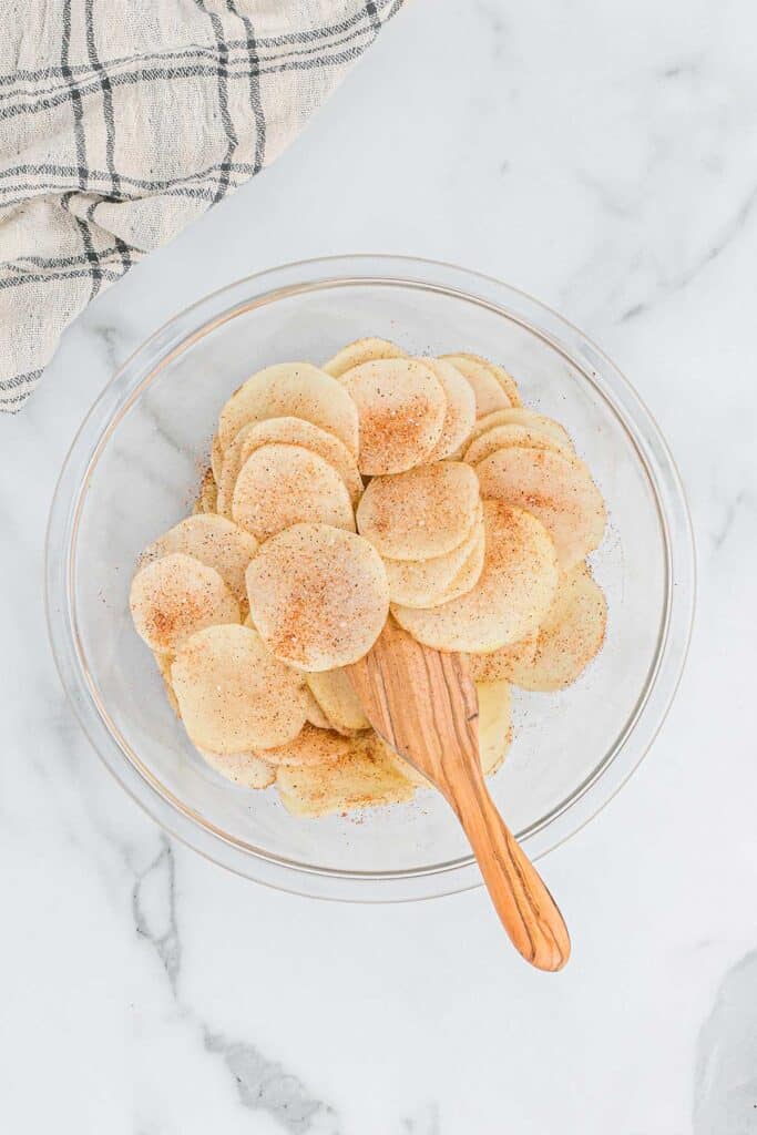 Potatoes in a bowl with seasoning mixture sprinkled over the top on a white countertop