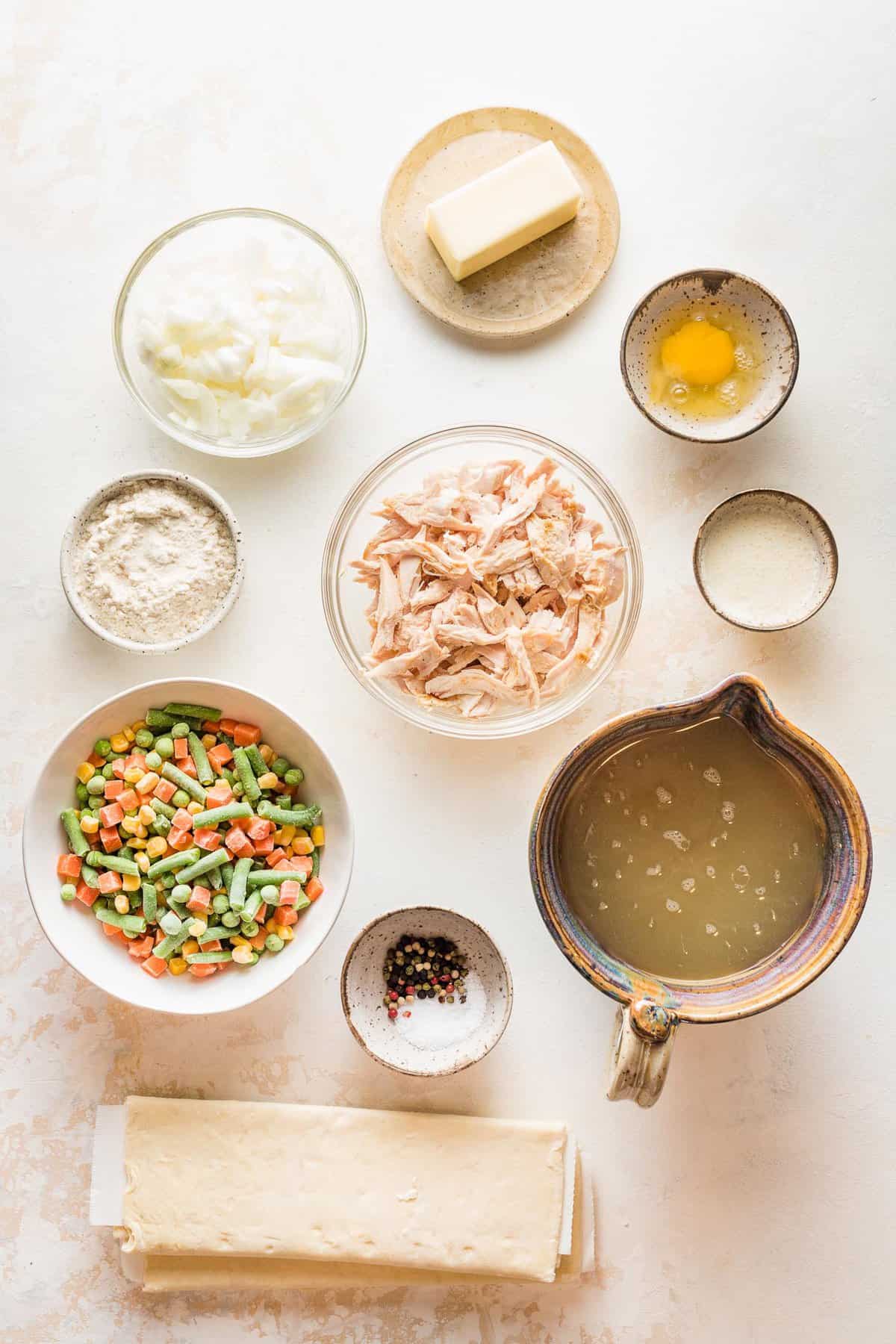 Ingredients to make turkey pot pie in small bowls on a white surface.